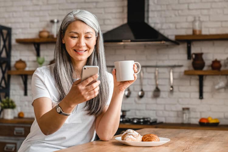 A woman making a dentist appointment on her phone while holding a coffee